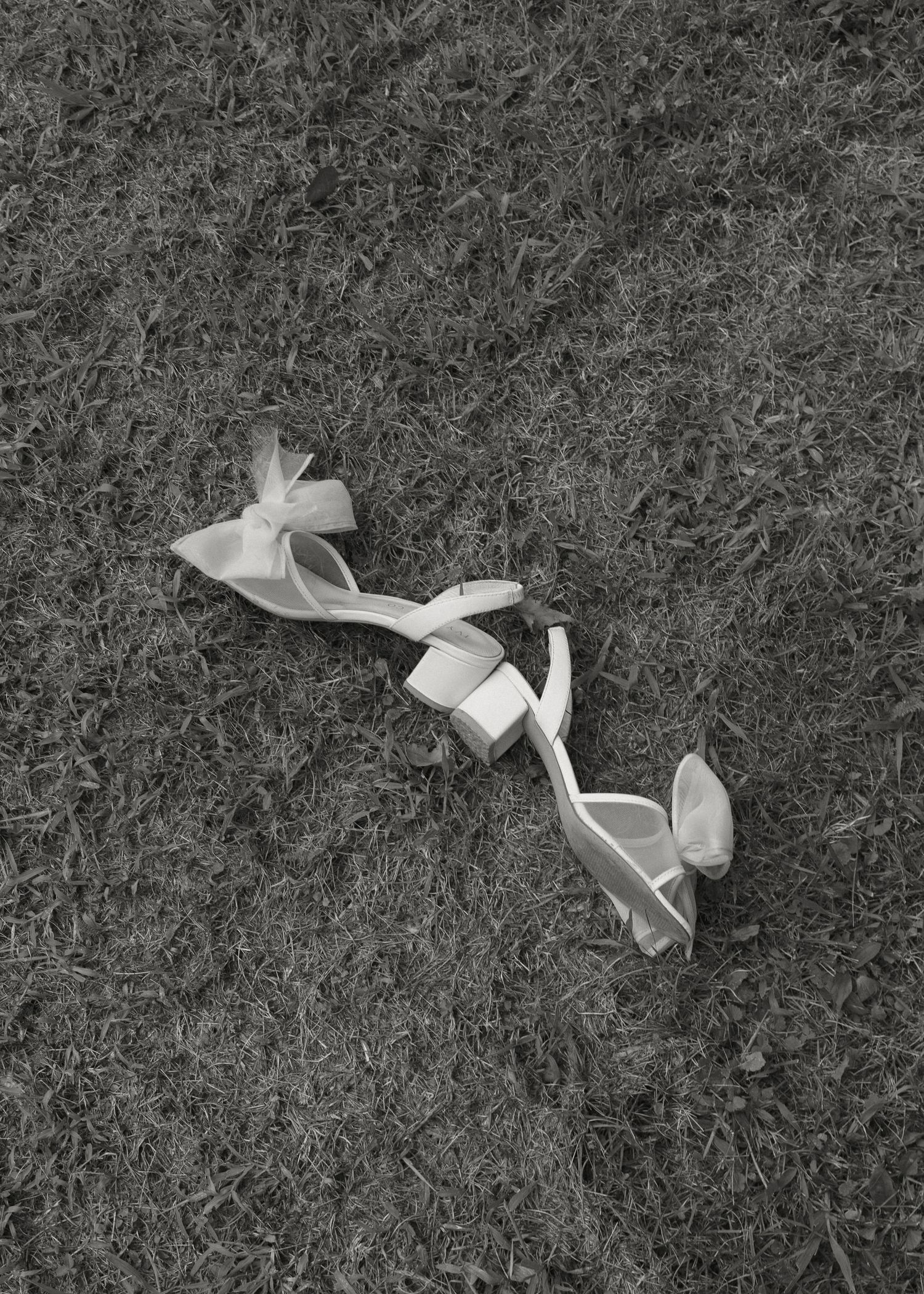 White bridal heels lying on green grass in black and white photography.