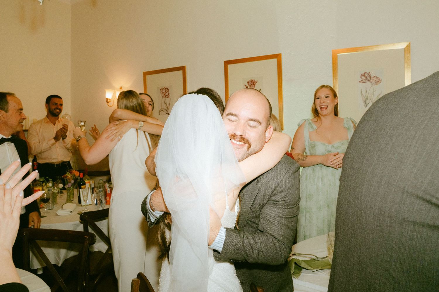 Groom smiling as bride hugs him warmly during joyful wedding reception celebration.