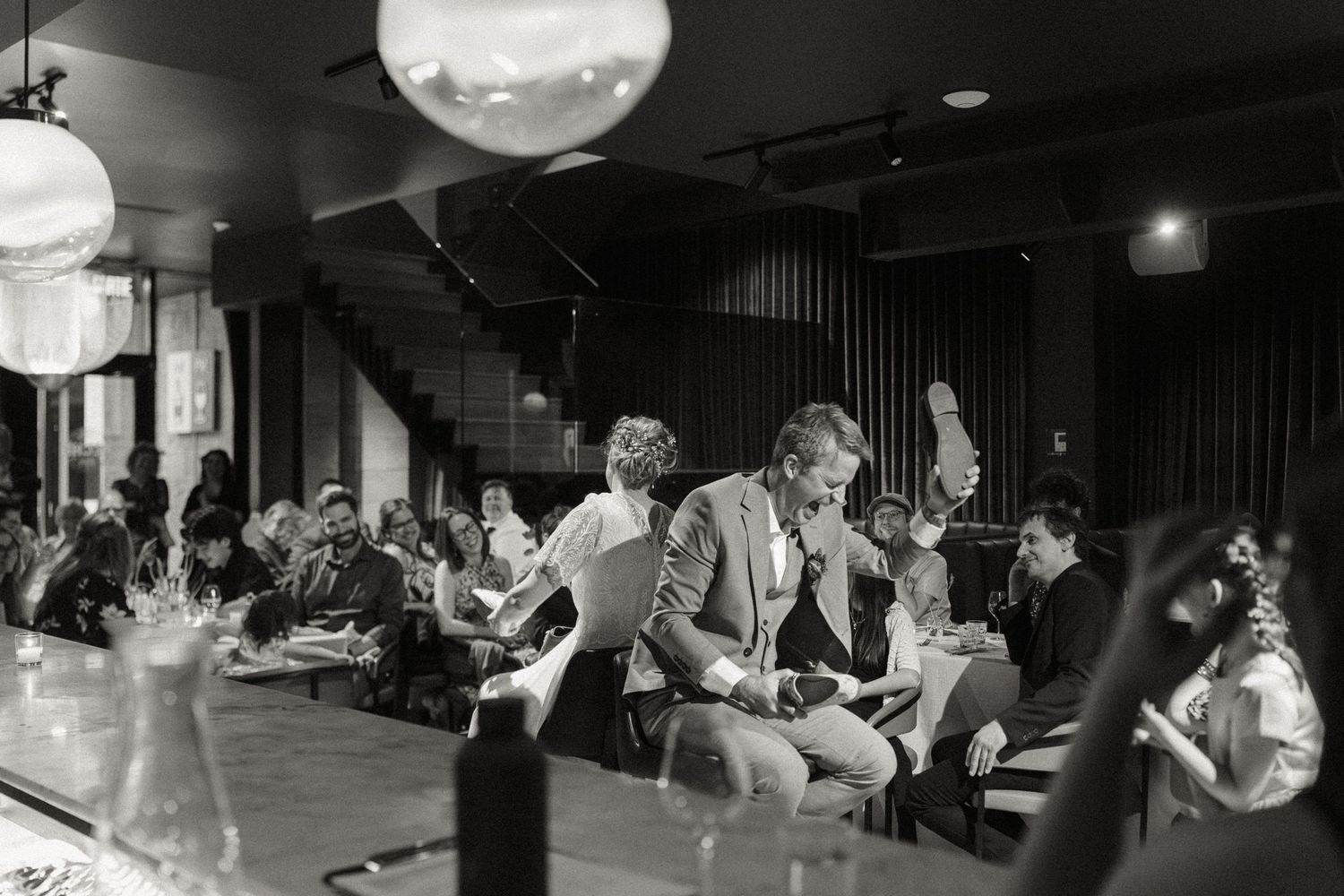 Wedding guests dancing and celebrating at elegant restaurant reception in black and white.