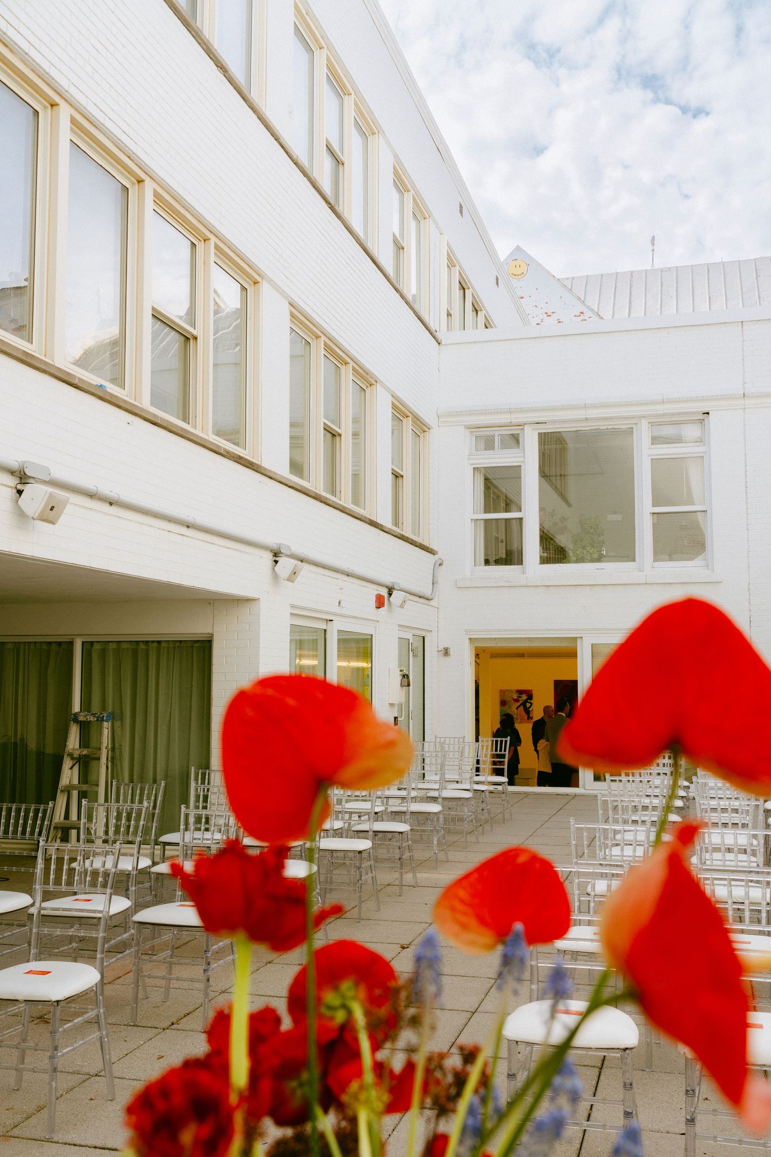 Outdoor courtyard wedding venue with white walls, rows of chairs, and vibrant red poppy flowers in the foreground.