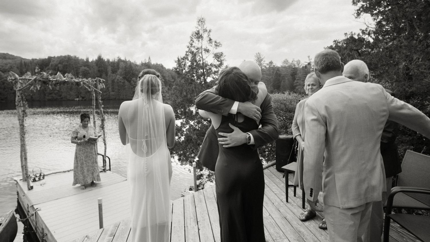 Bride and groom share an emotional embrace on a lakeside dock during their outdoor wedding ceremony.