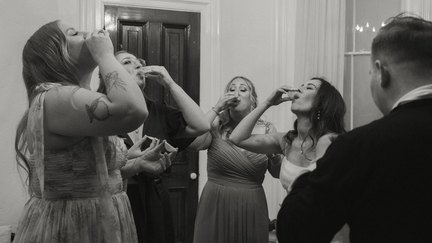 Bridesmaids in blue dresses taking celebratory shots together at a wedding reception.