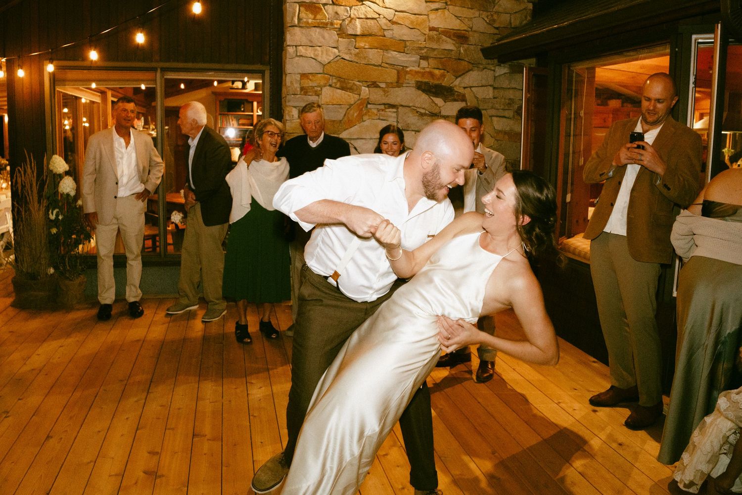 Groom dipping bride in elegant white gown during first dance at wedding reception.