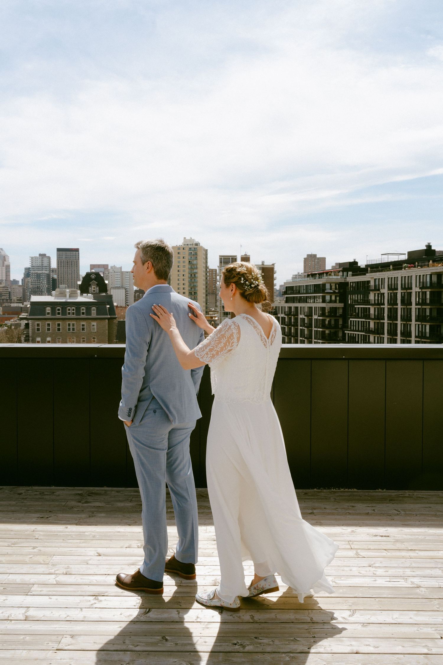Bride and groom share a romantic first look on a rooftop with a city skyline backdrop.