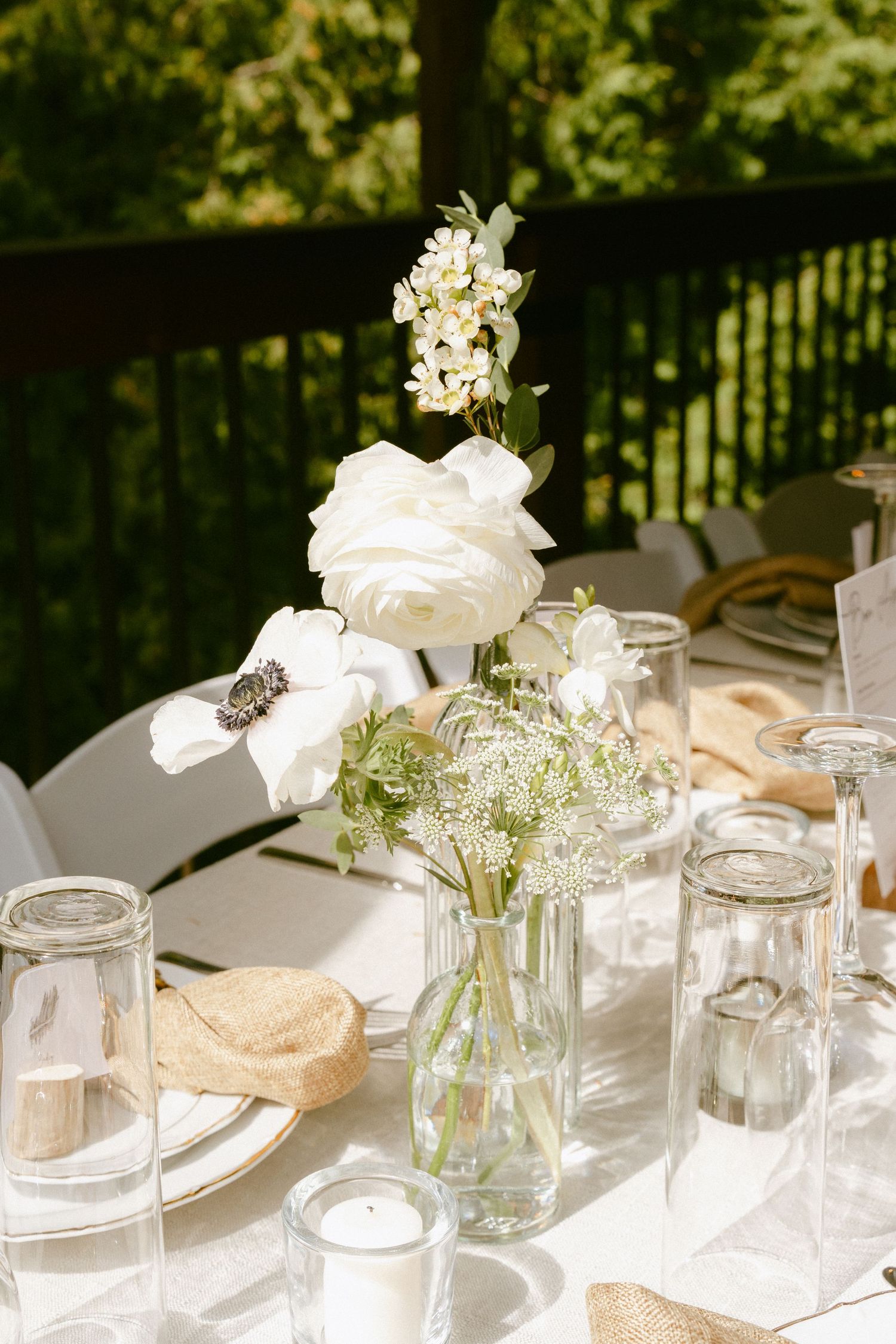 White anemone and ranunculus floral centerpiece in glass jar vases on an outdoor wedding reception table.
