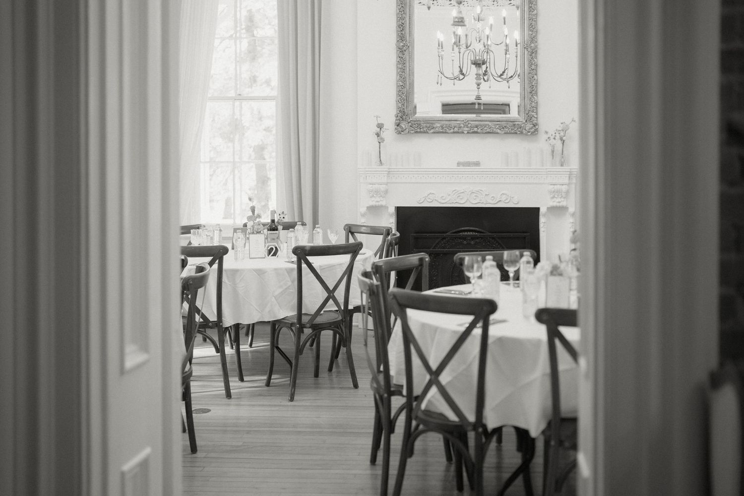 Black and white photo of a sophisticated wedding reception room with fireplace and chandelier decor.