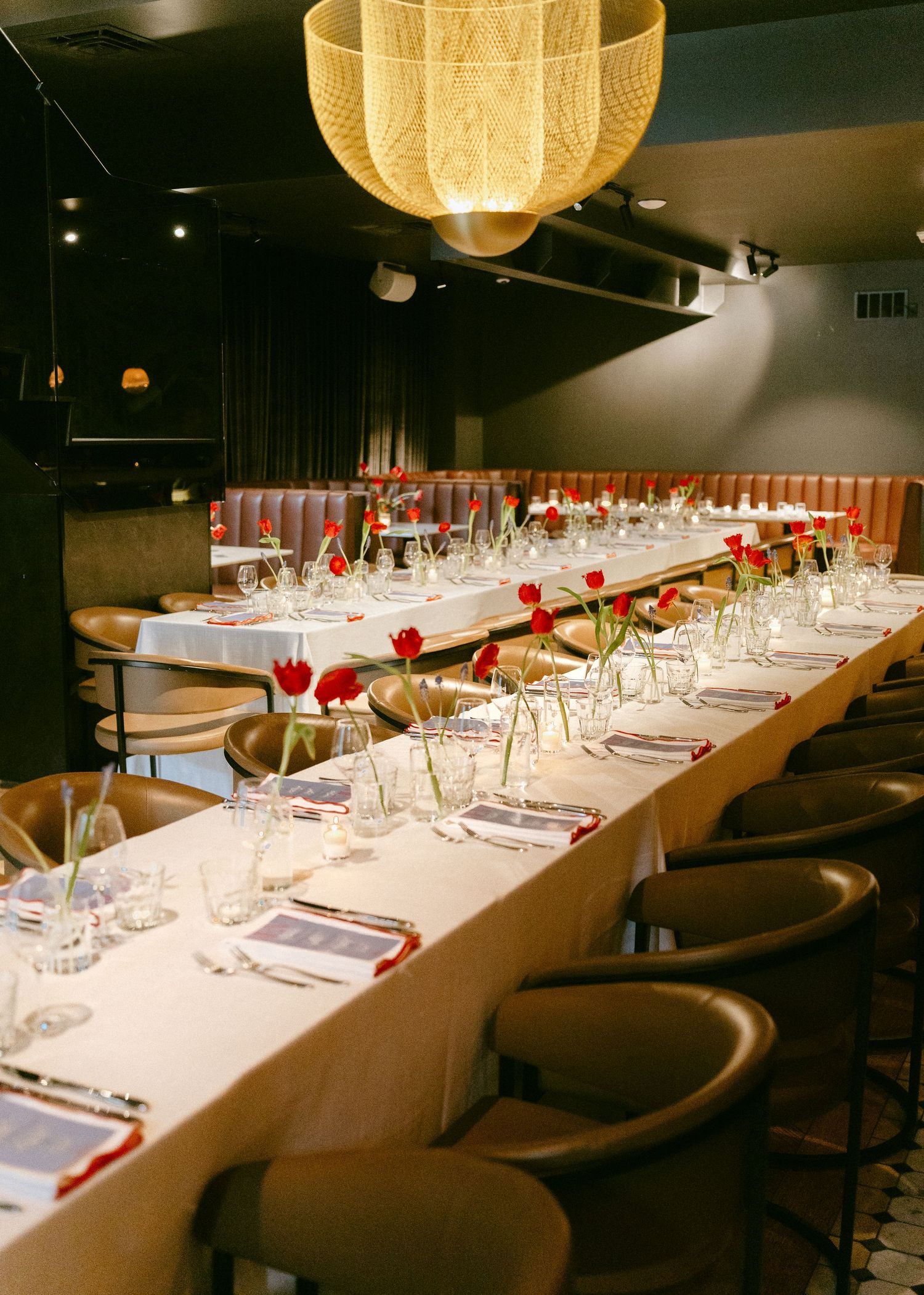 Long wedding reception dinner table with red tulip centerpieces under woven pendant light.