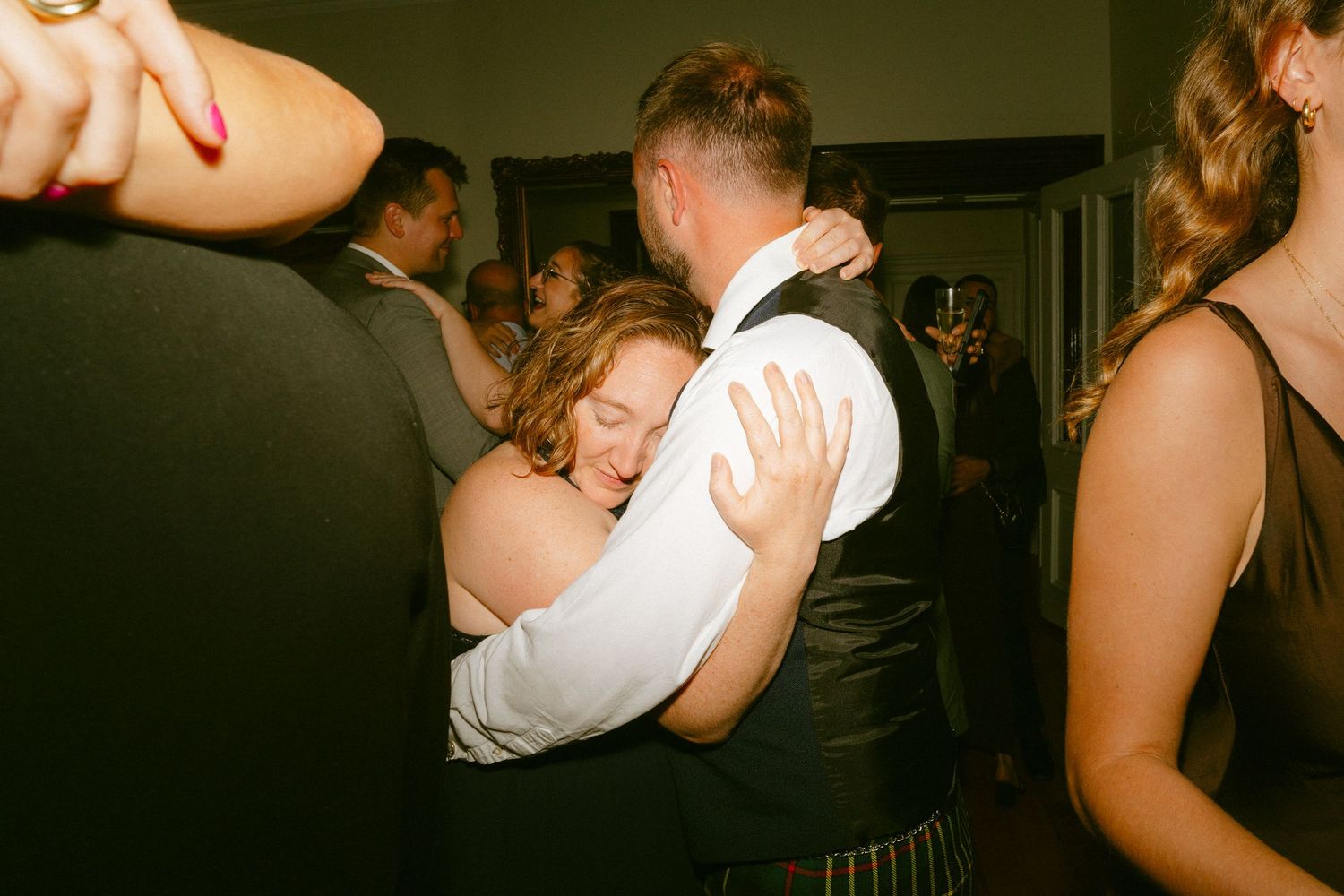 Wedding guest in strapless dress embraces a man in a kilt on the dance floor.