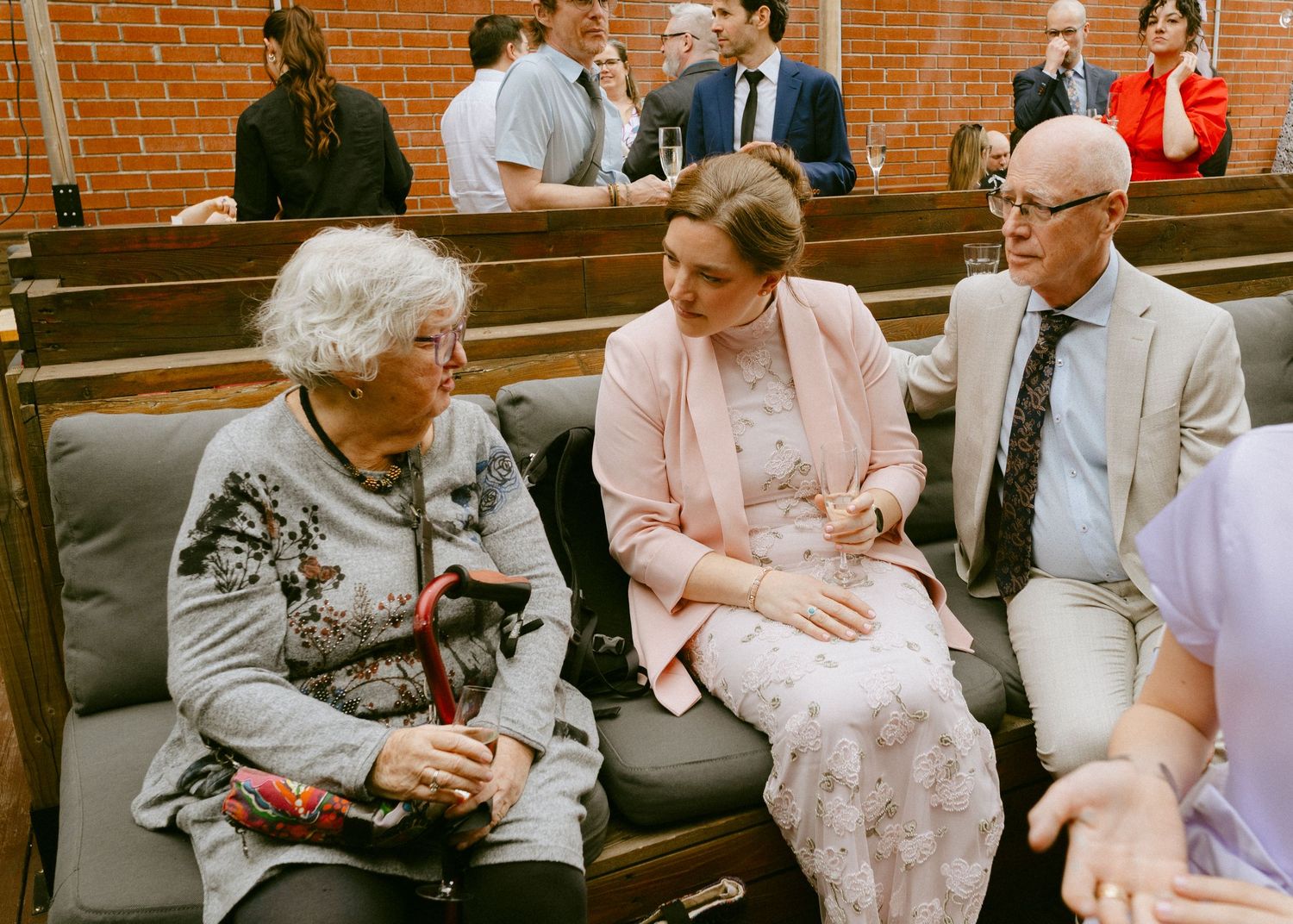 Three elderly guests chat on church pew bench at wedding ceremony reception.