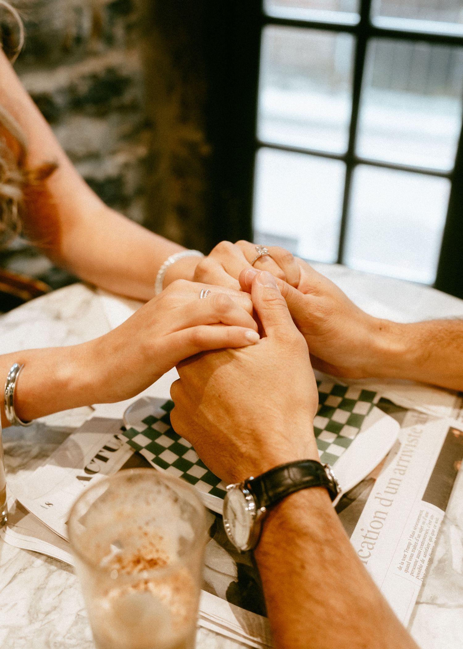 Couple holding hands tenderly across a checkered tablecloth at a romantic restaurant dinner.