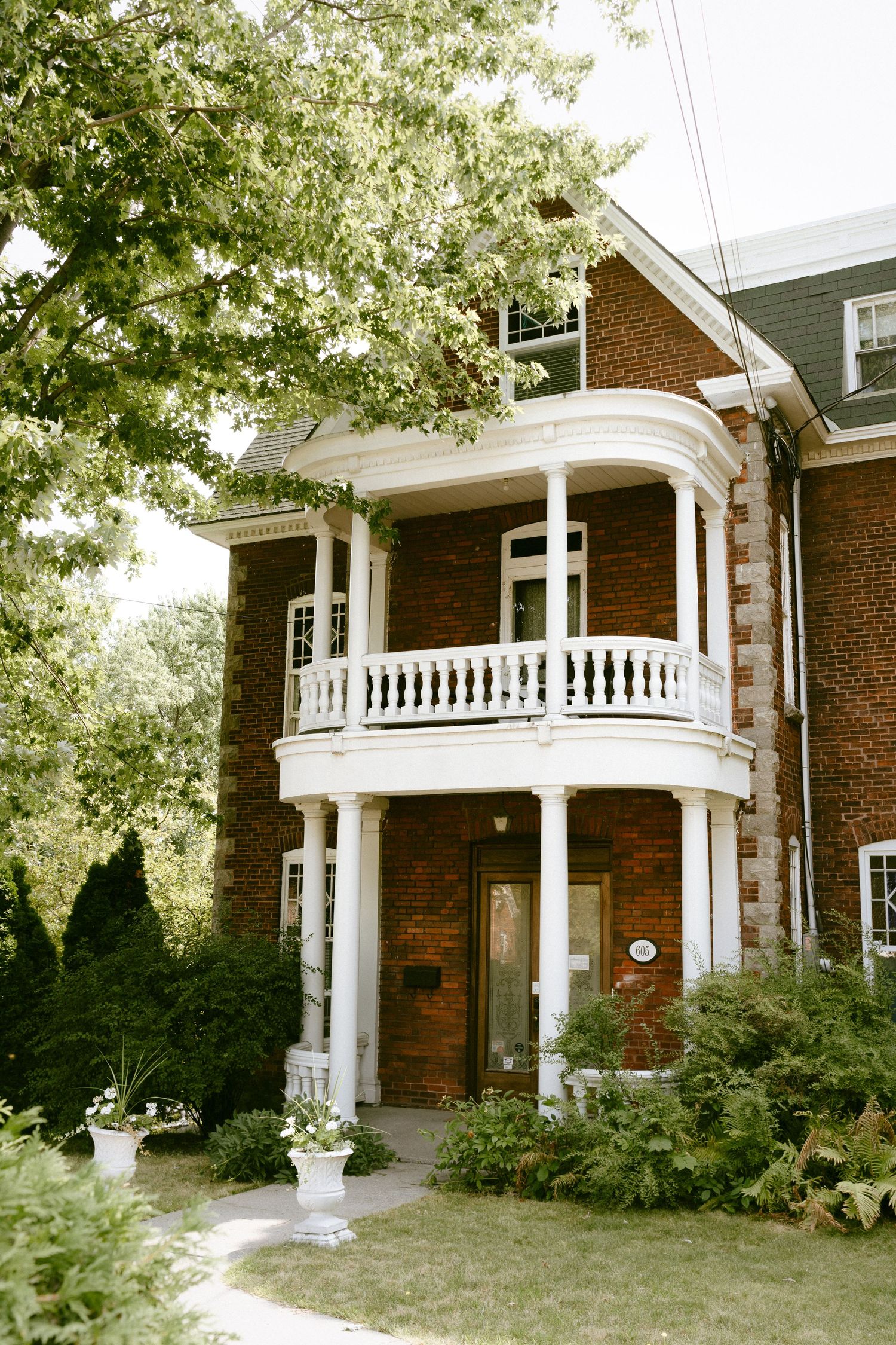 A charming red brick Victorian home with white balcony columns and lush greenery.