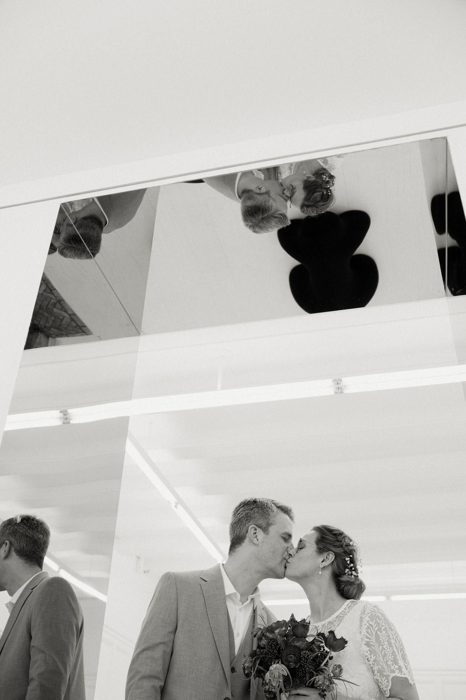 Black and white photo of bride and groom sharing a kiss beneath mirrored ceiling at wedding venue.