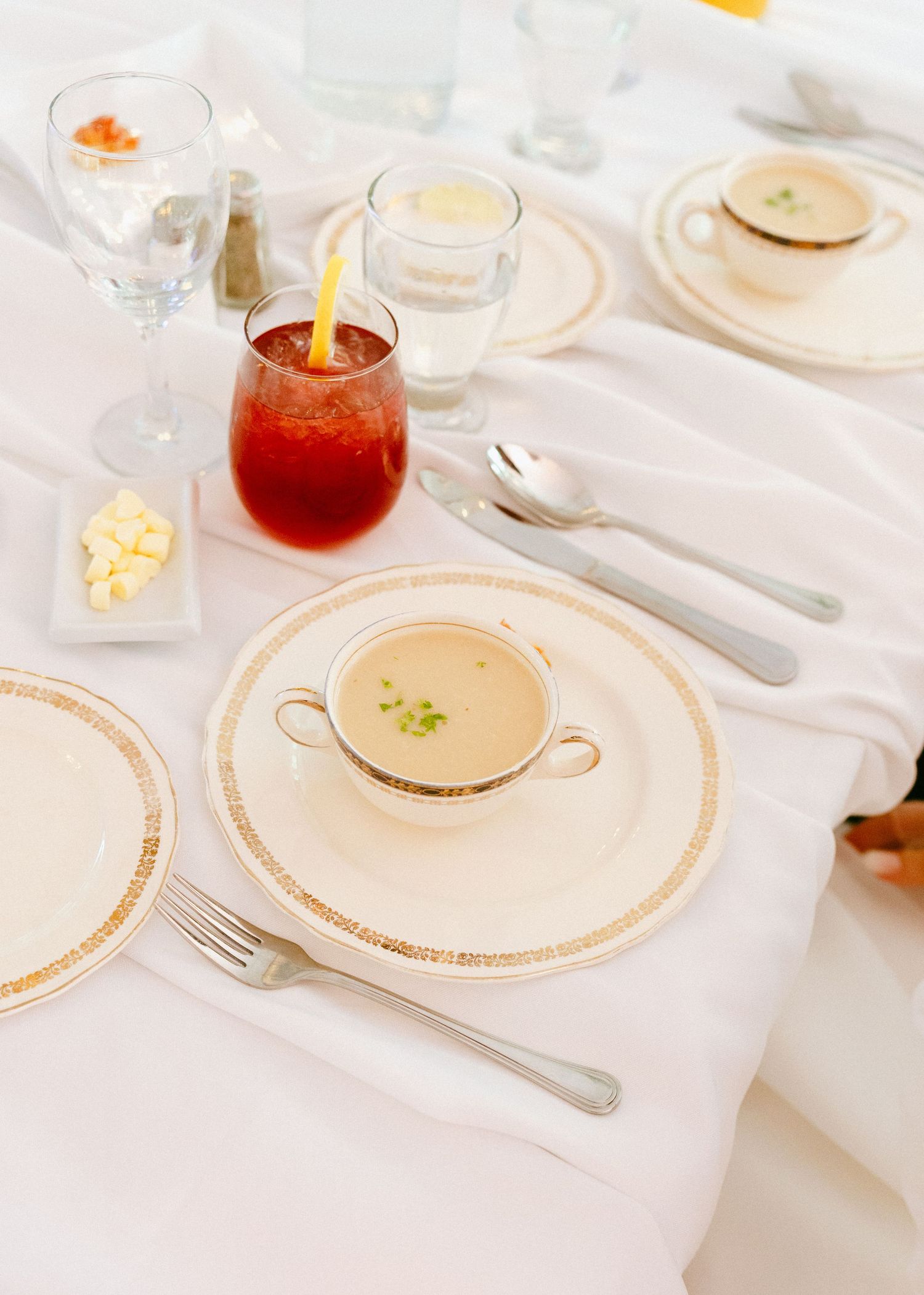 Elegant wedding reception place setting with soup course, red cocktail, and gold-rimmed china.