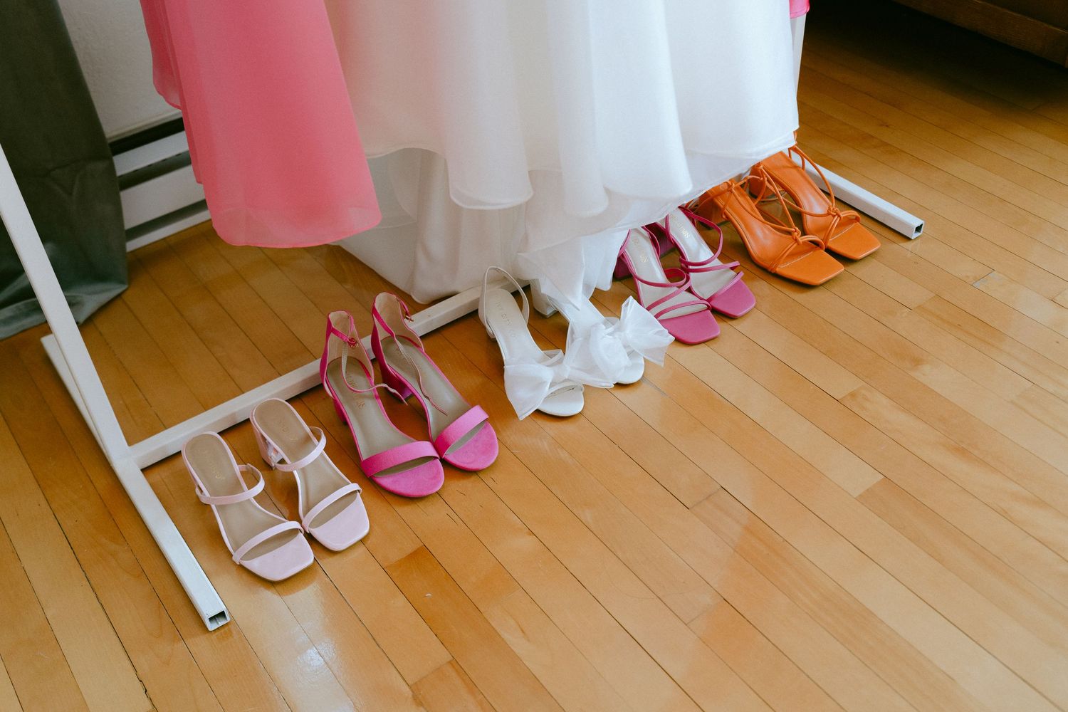 Colorful wedding party heels in pink, white, and orange arranged beneath bridal gowns.