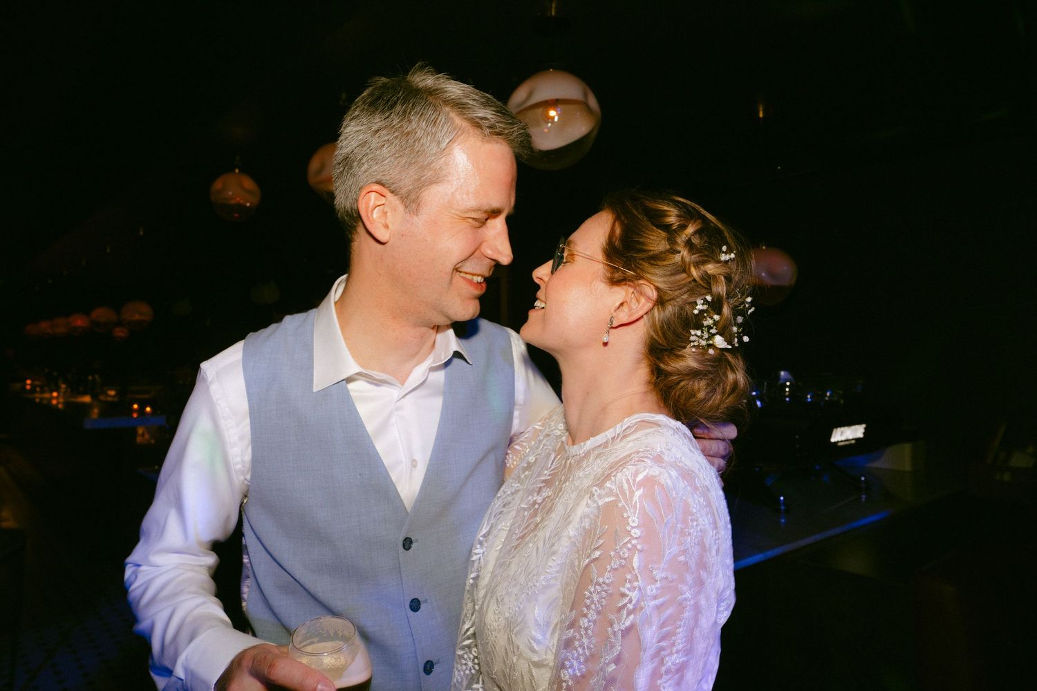 A couple shares a romantic moment at a wedding reception in dim lighting.