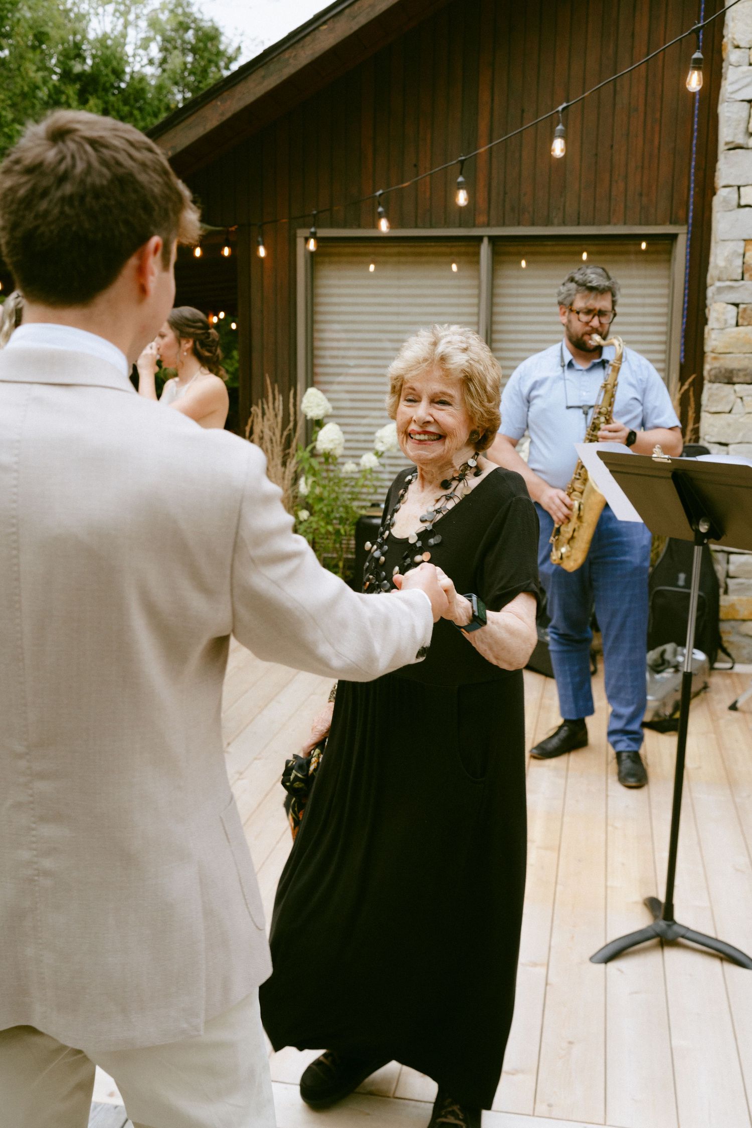 Guest dancing with smiling woman in black dress at outdoor wedding reception.