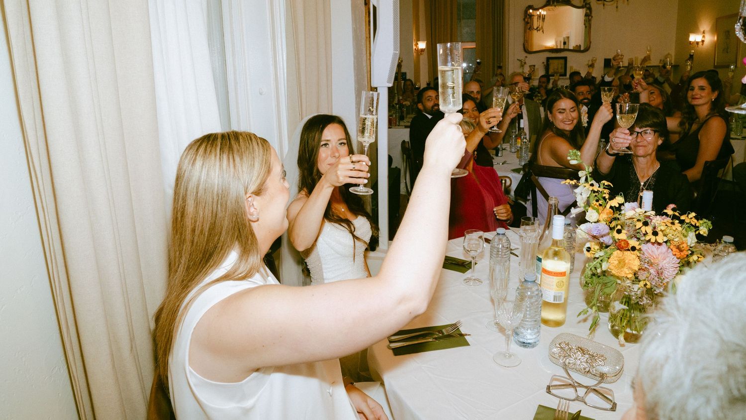 Wedding guests raising champagne glasses in a toast at elegant floral reception table.