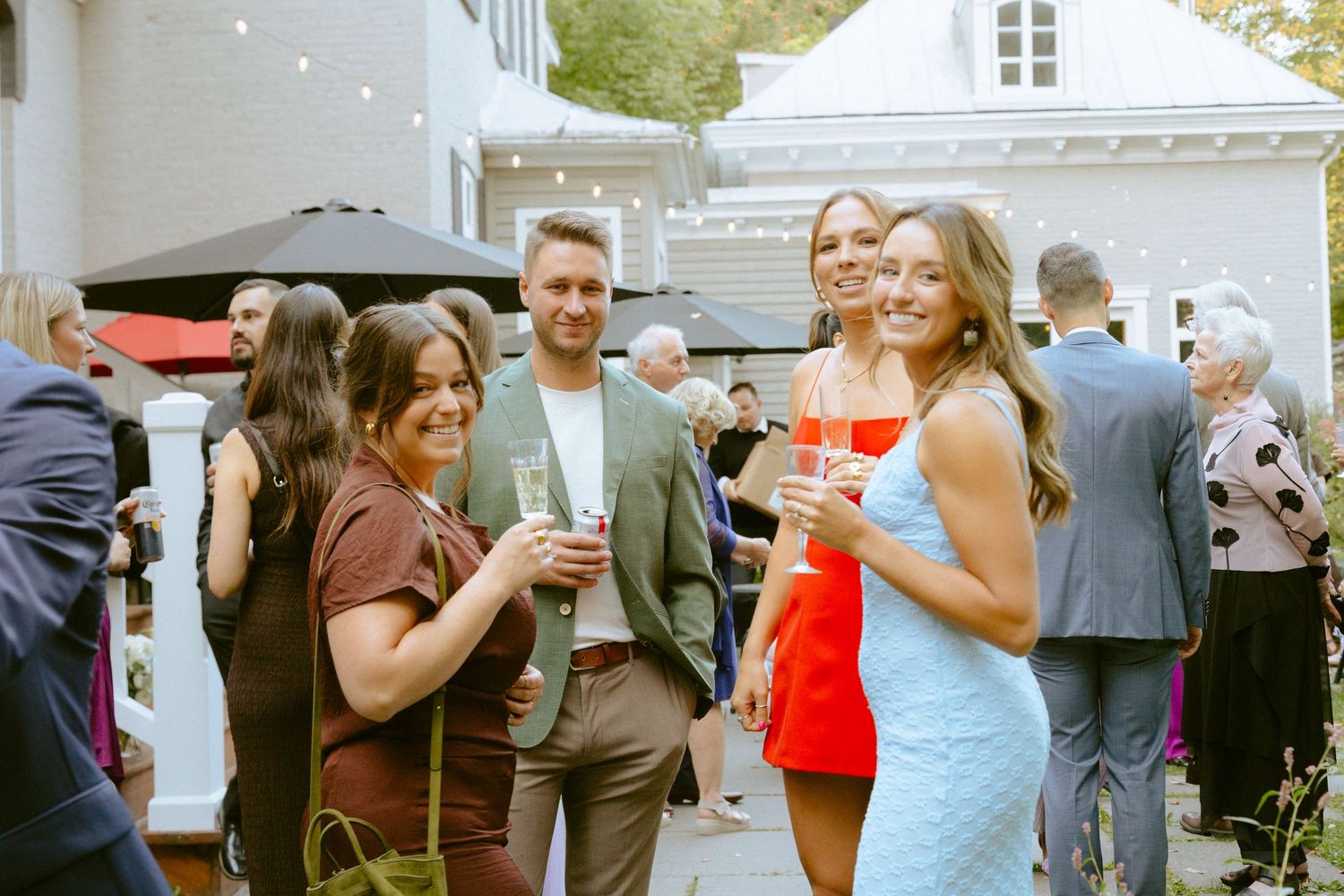 Four smiling wedding guests holding champagne pose together outdoors at an elegant evening reception.