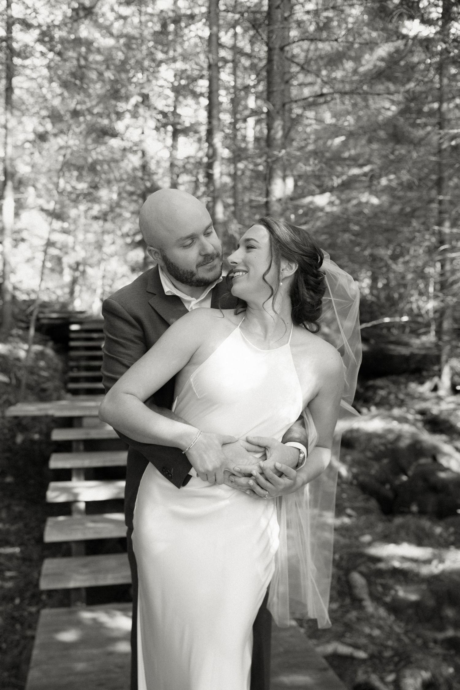 Bride and groom embracing and smiling in black and white forest wedding portrait.