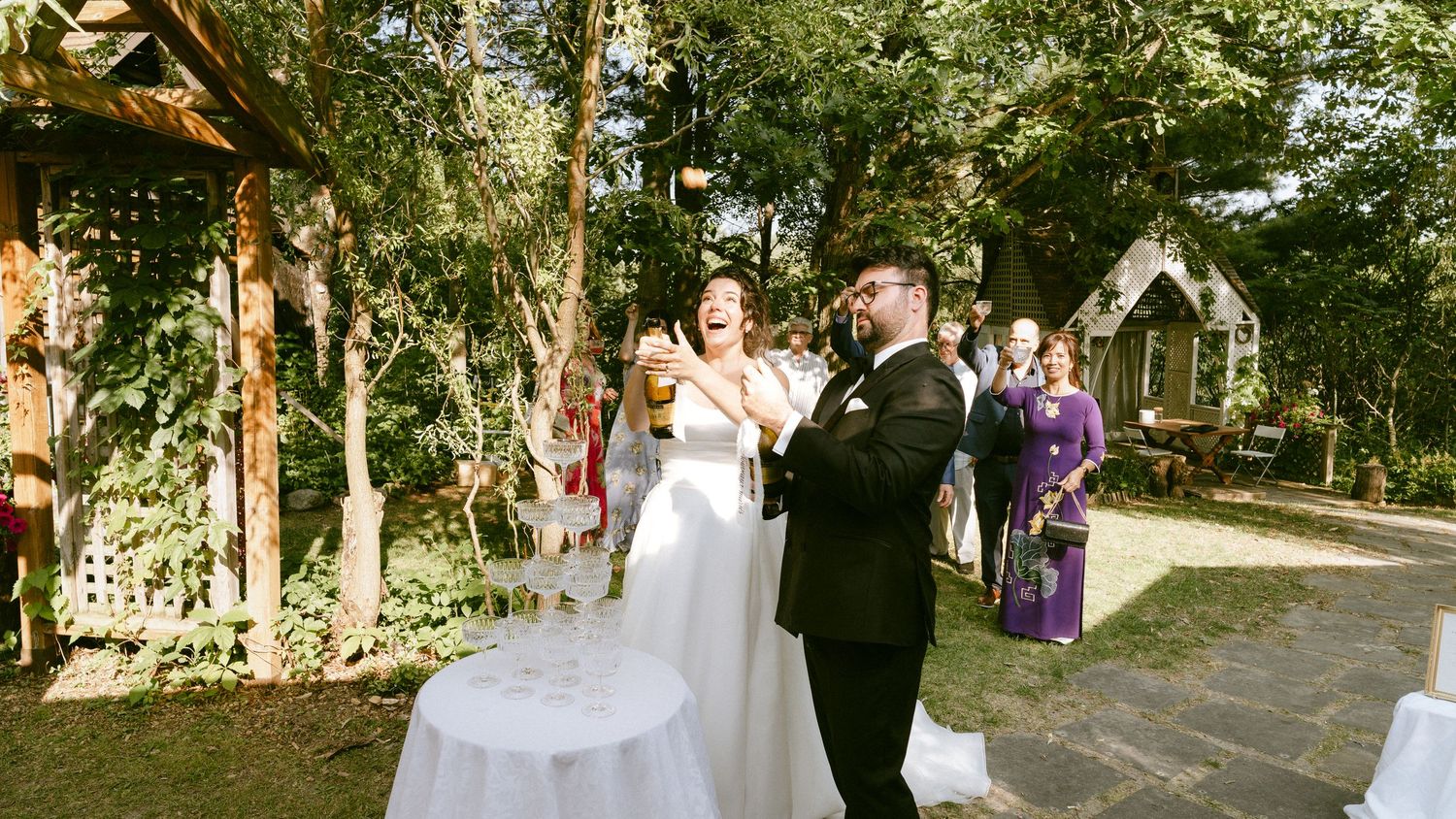 Bride and groom celebrate with champagne toast at an elegant outdoor garden wedding reception.