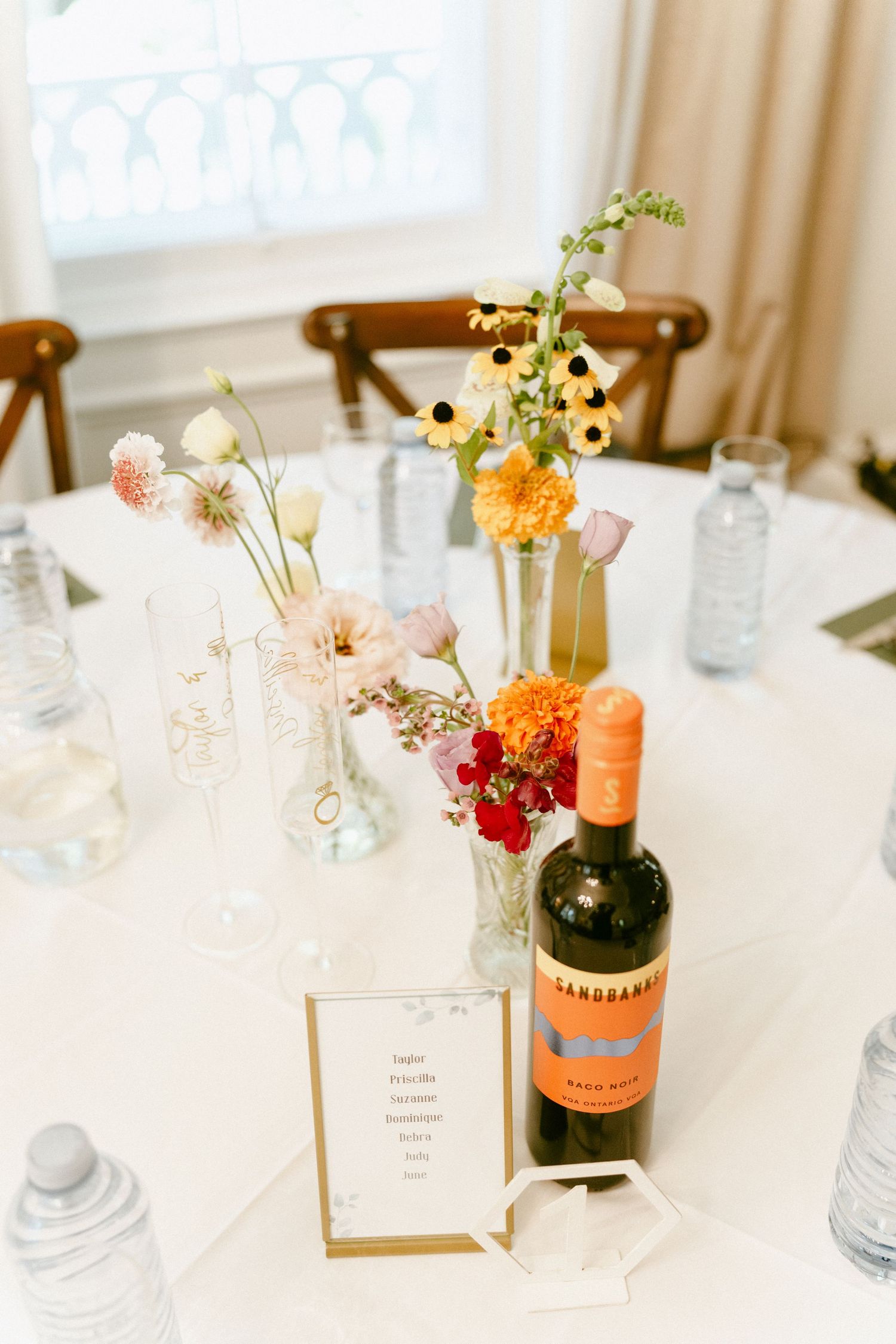 Wedding reception table with colorful wildflower centerpieces, a wine bottle, and a seating card.