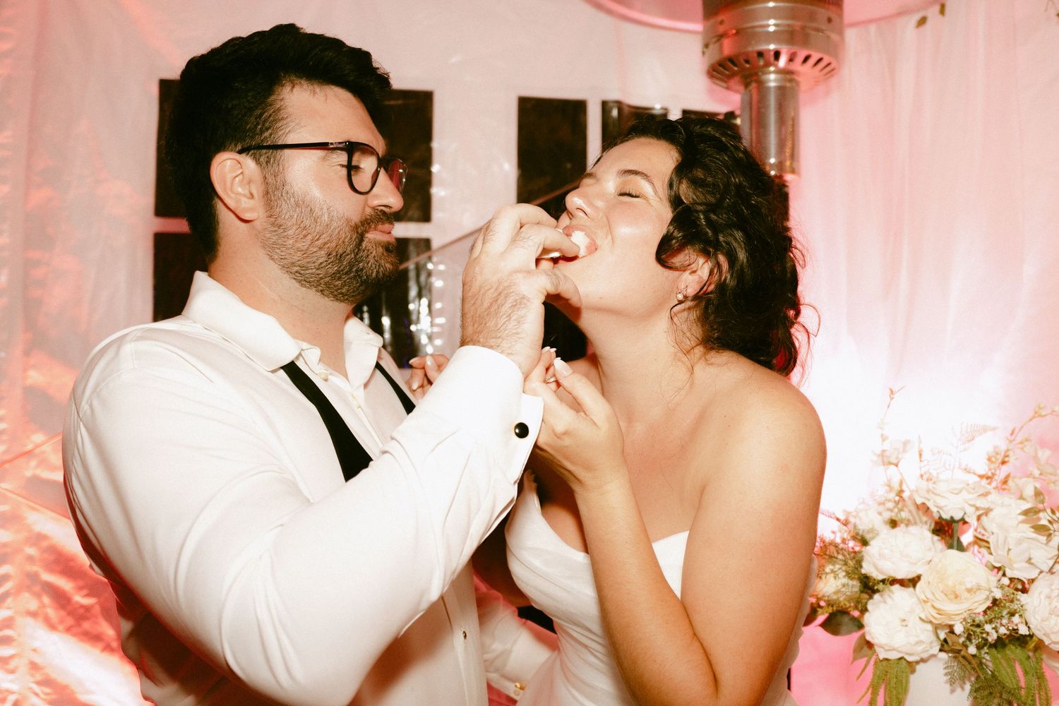 Groom feeding bride wedding cake at romantic reception celebration.