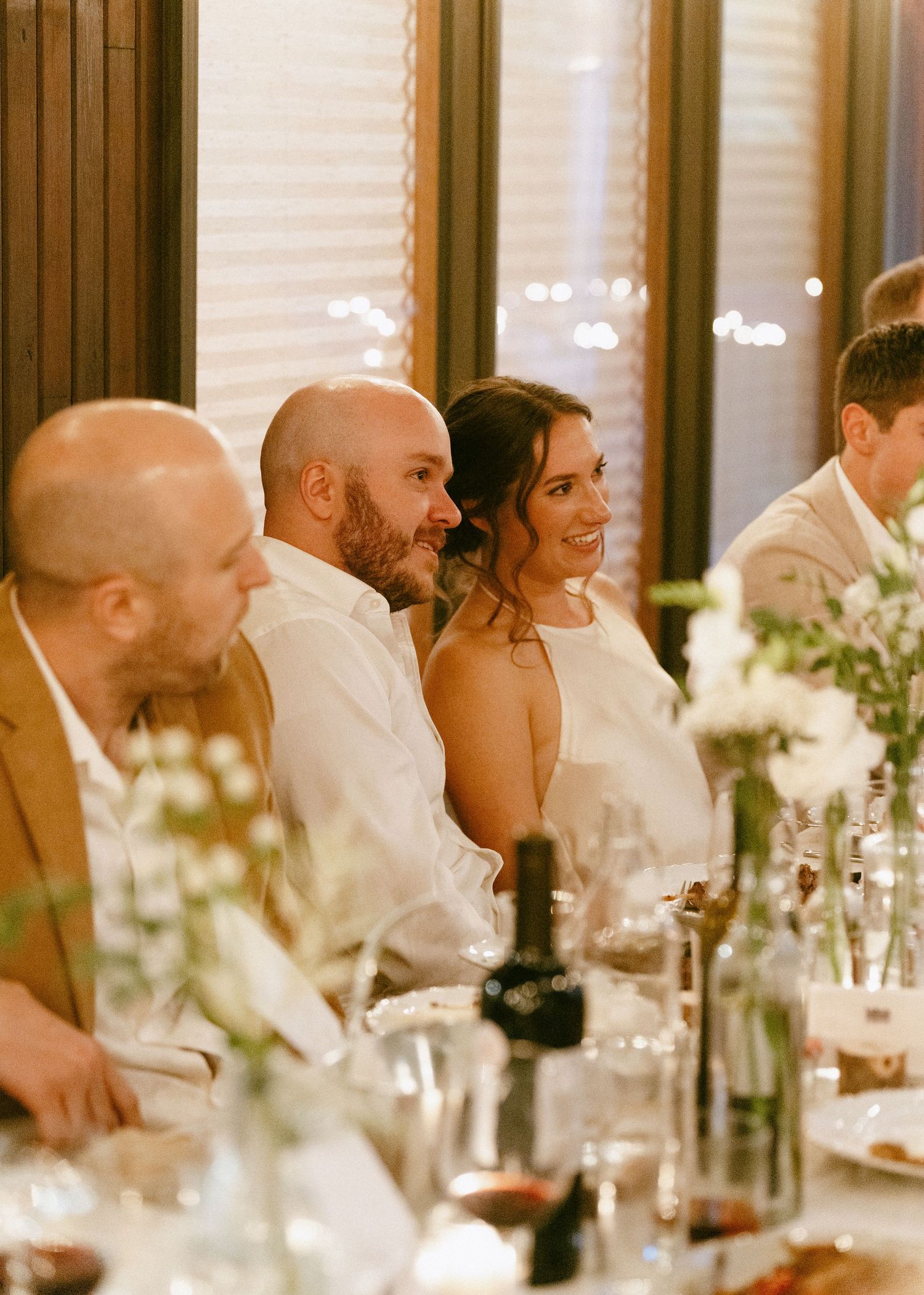 Bride and groom smiling warmly at their wedding reception dinner table with floral centerpieces.