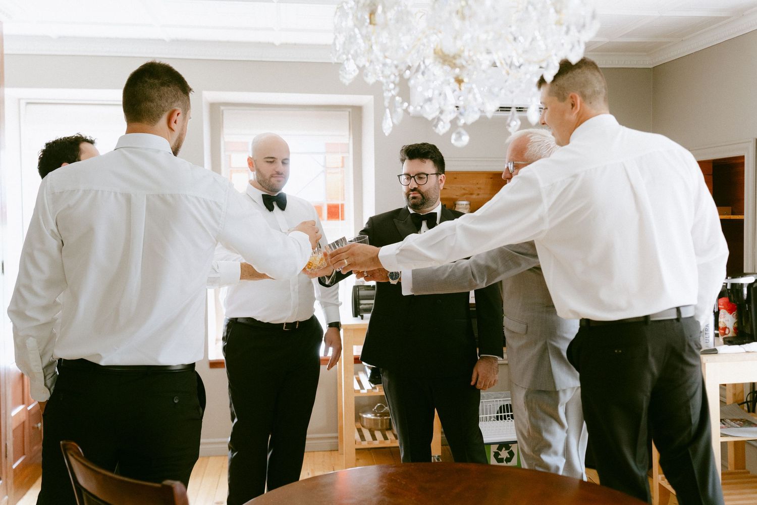 Groomsmen in formal attire sharing a group handshake huddle during wedding day preparations.