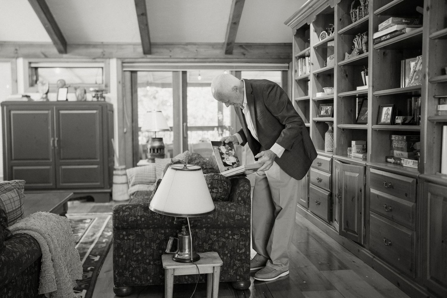 Elderly man in suit adjusting cufflinks in rustic cabin living room before wedding.
