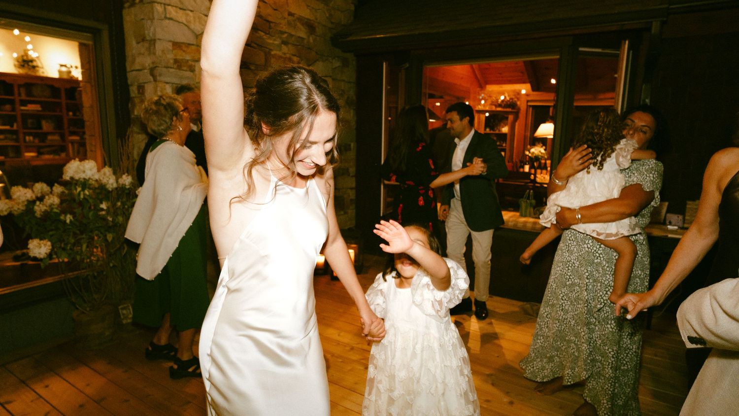Bride in white gown dancing with young flower girl at wedding reception.