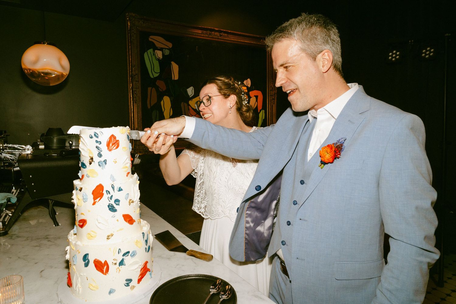Bride and groom cutting elegant white wedding cake with colorful floral decorations.