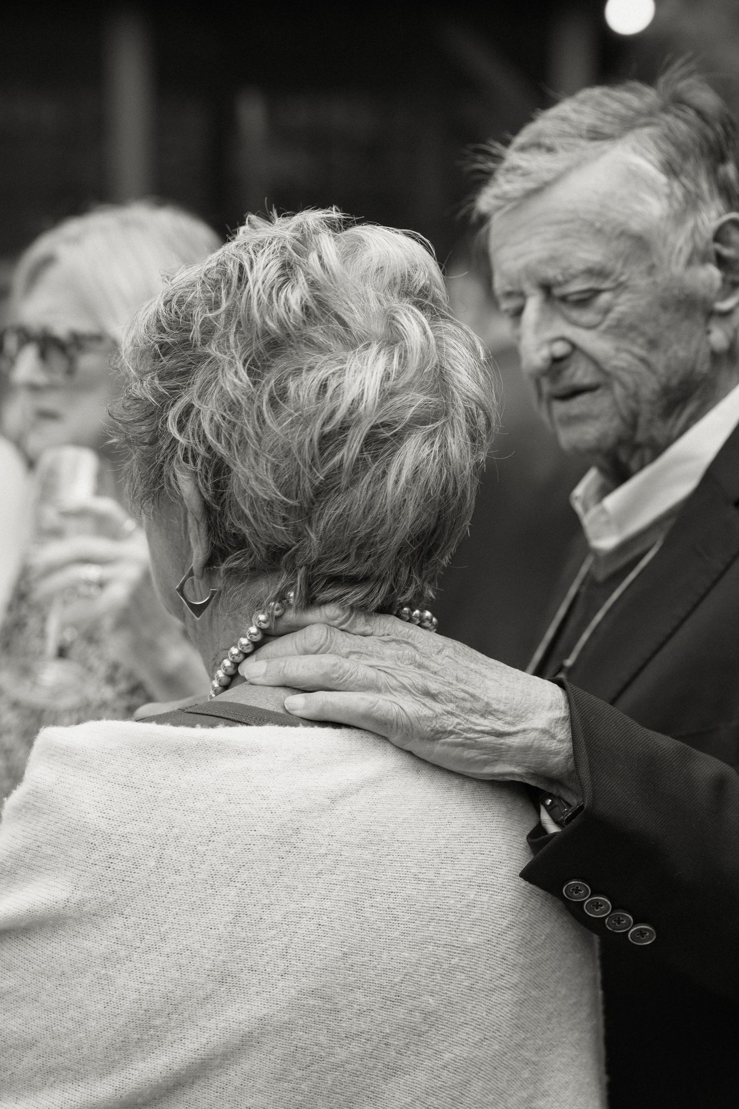 Elderly man gently placing hand on woman's shoulder in tender black and white wedding photo.