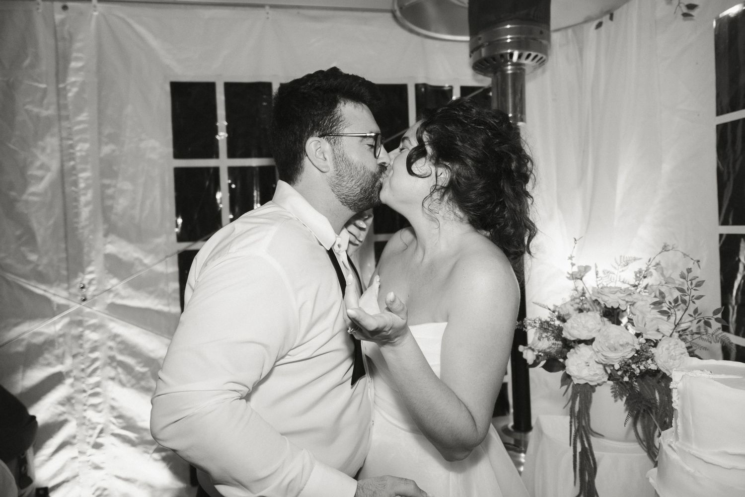 Black and white photo of bride and groom kissing at cake cutting.