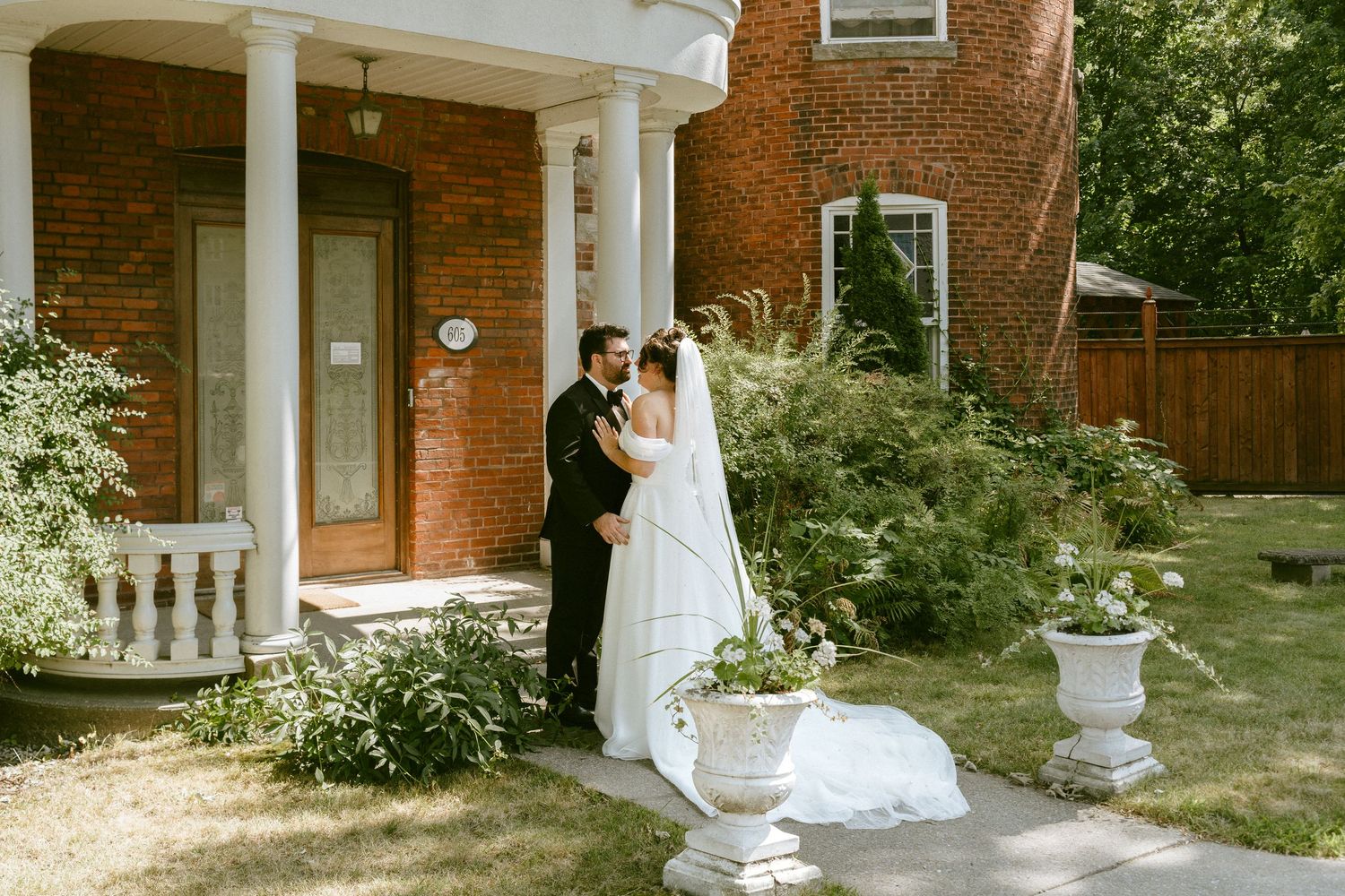 Bride and groom pose together in front of elegant red brick manor with lush gardens.