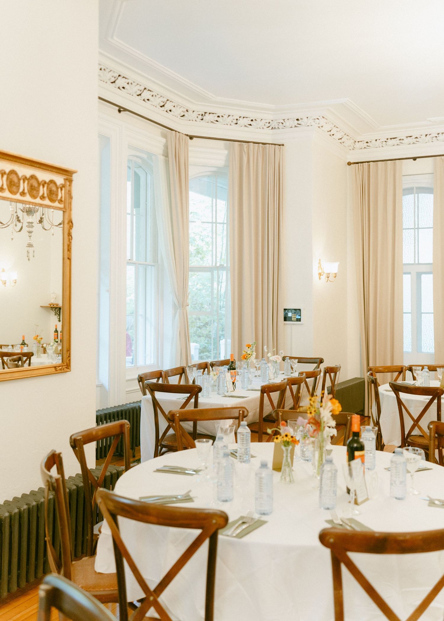 Elegant wedding reception dining room with white tablecloths, wooden chairs, and floral centerpieces.
