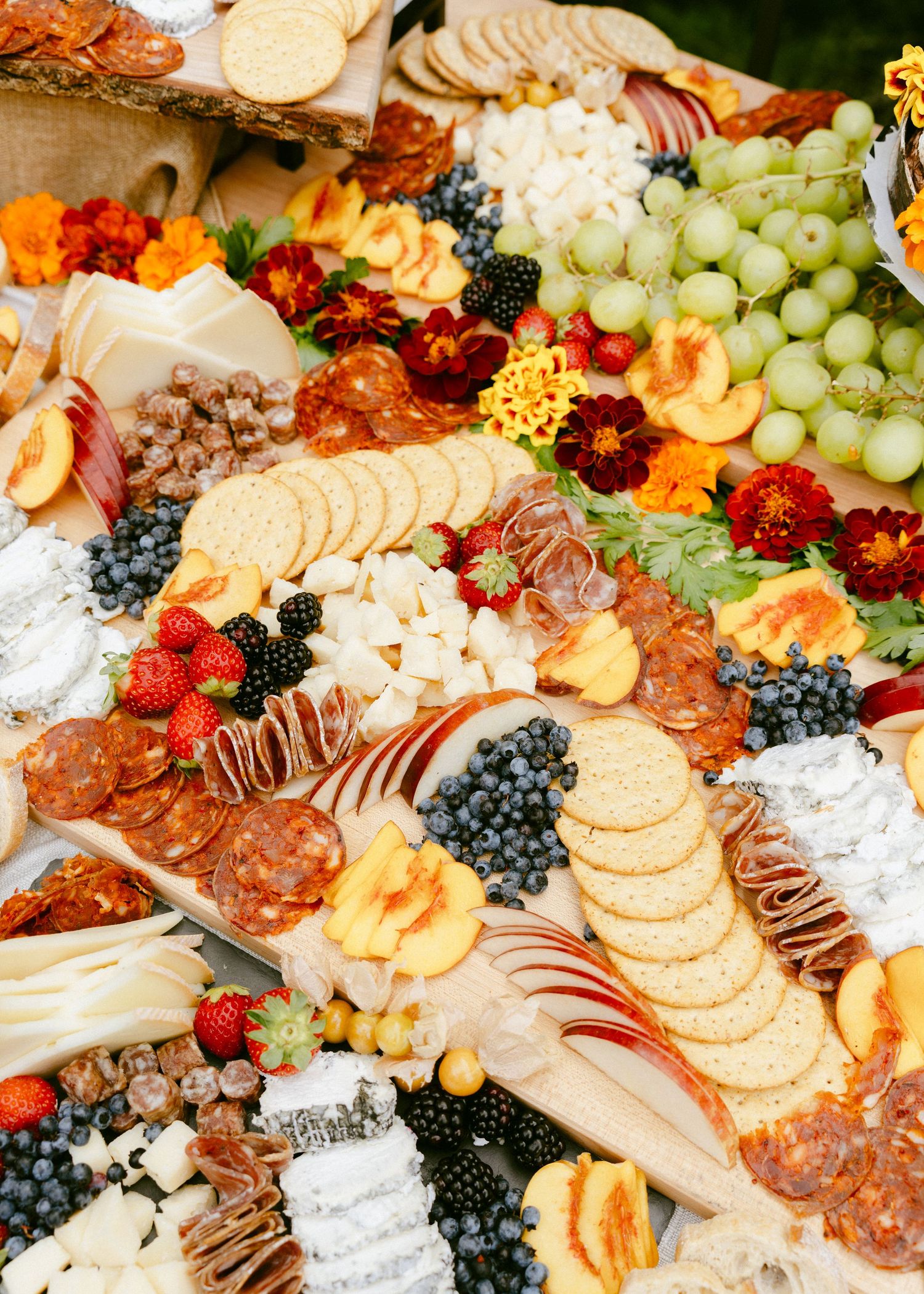 Close-up of a stunning wedding grazing board with salami, cheeses, grapes, peaches, berries, and marigolds.