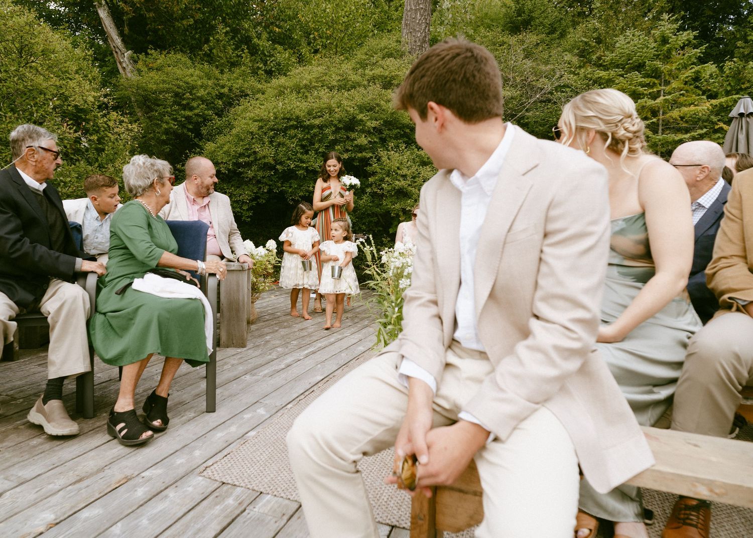 Wedding guests seated on wooden benches during an outdoor garden ceremony on a deck.