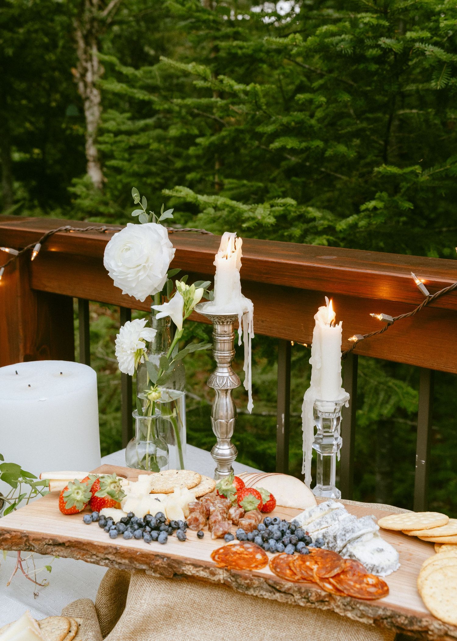 Elegant wedding charcuterie board with candles, white flowers, berries, and crackers on outdoor deck.