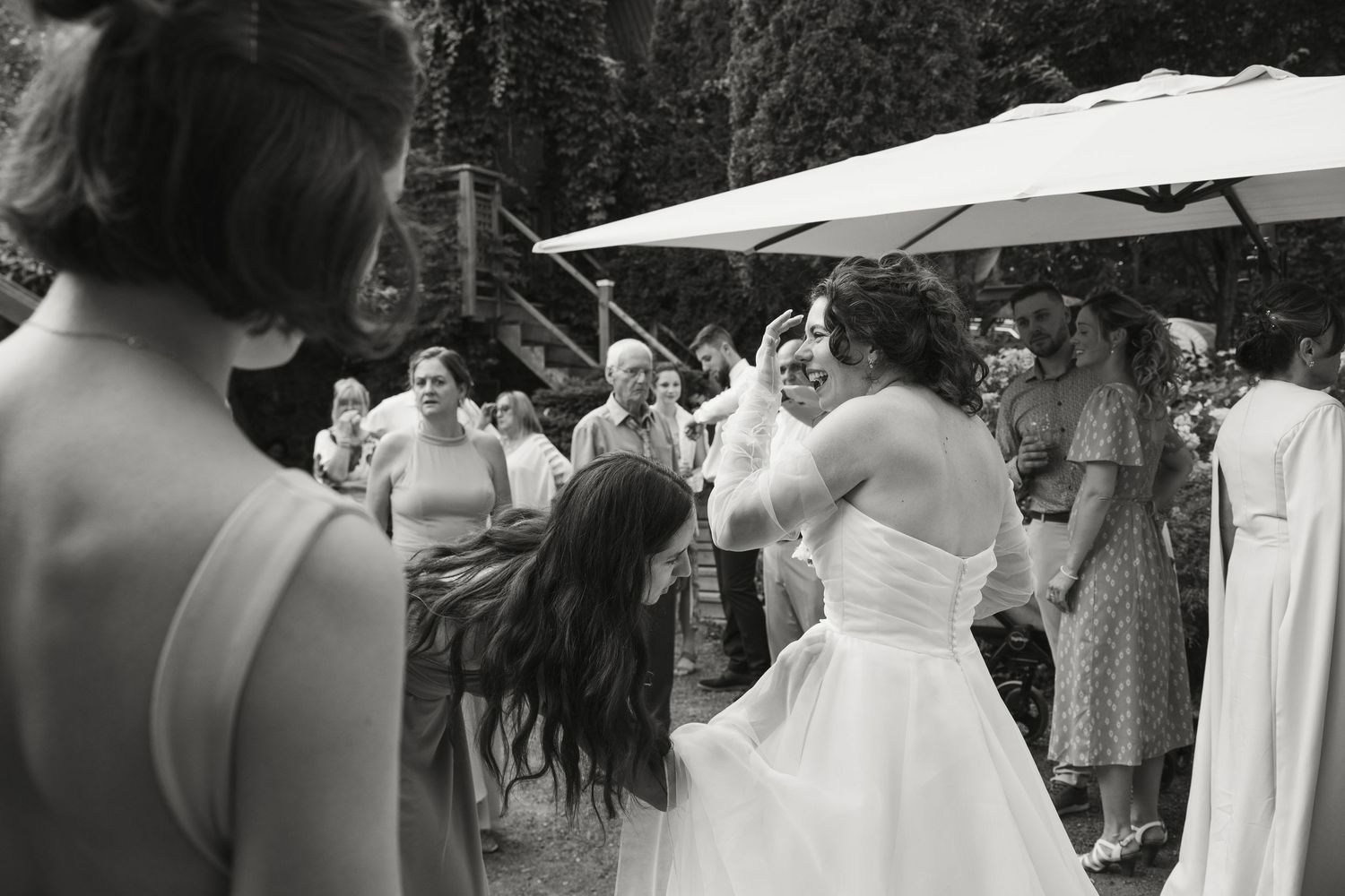 Black and white photo of bride in white gown dancing with guests at outdoor wedding reception.