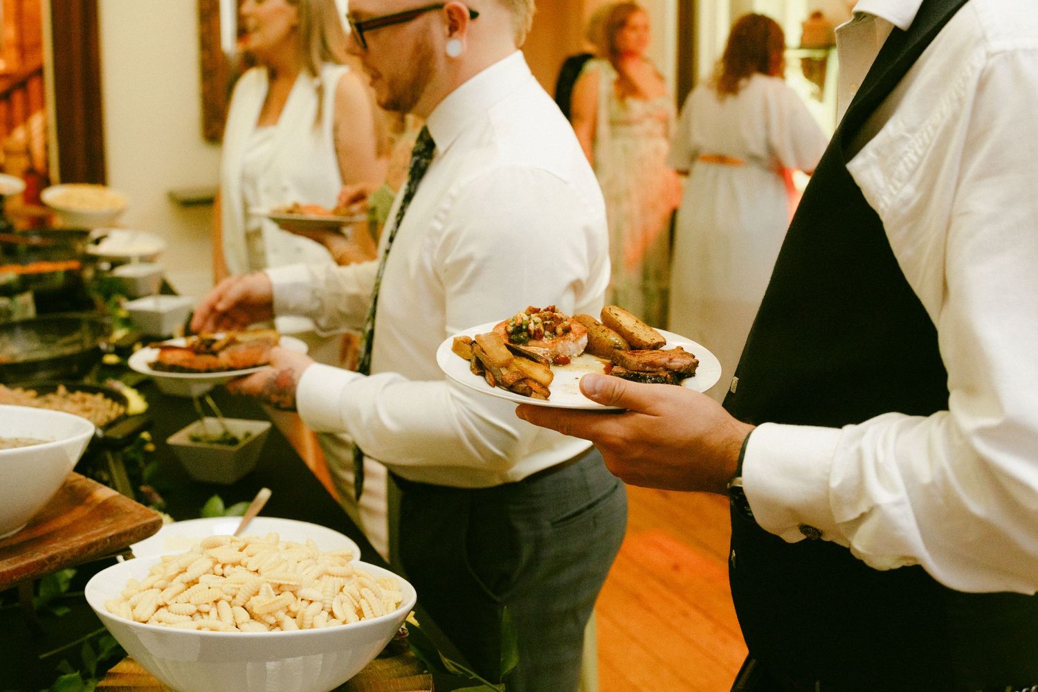 Catering staff serving food at a wedding reception buffet with elegant dishes.