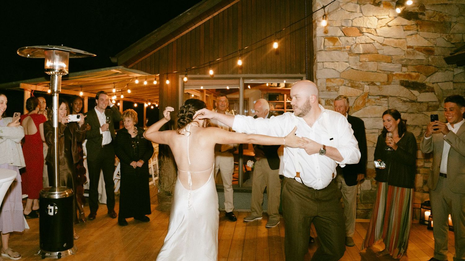 Bride and groom dancing together under string lights at outdoor evening wedding reception.