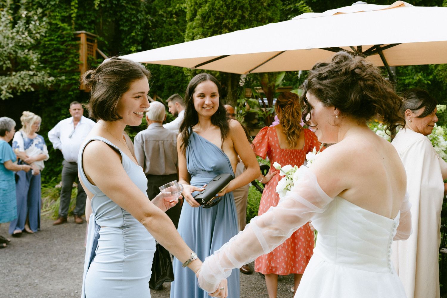 Bride in white gown holding hands with bridesmaid in blue dress at outdoor wedding reception.
