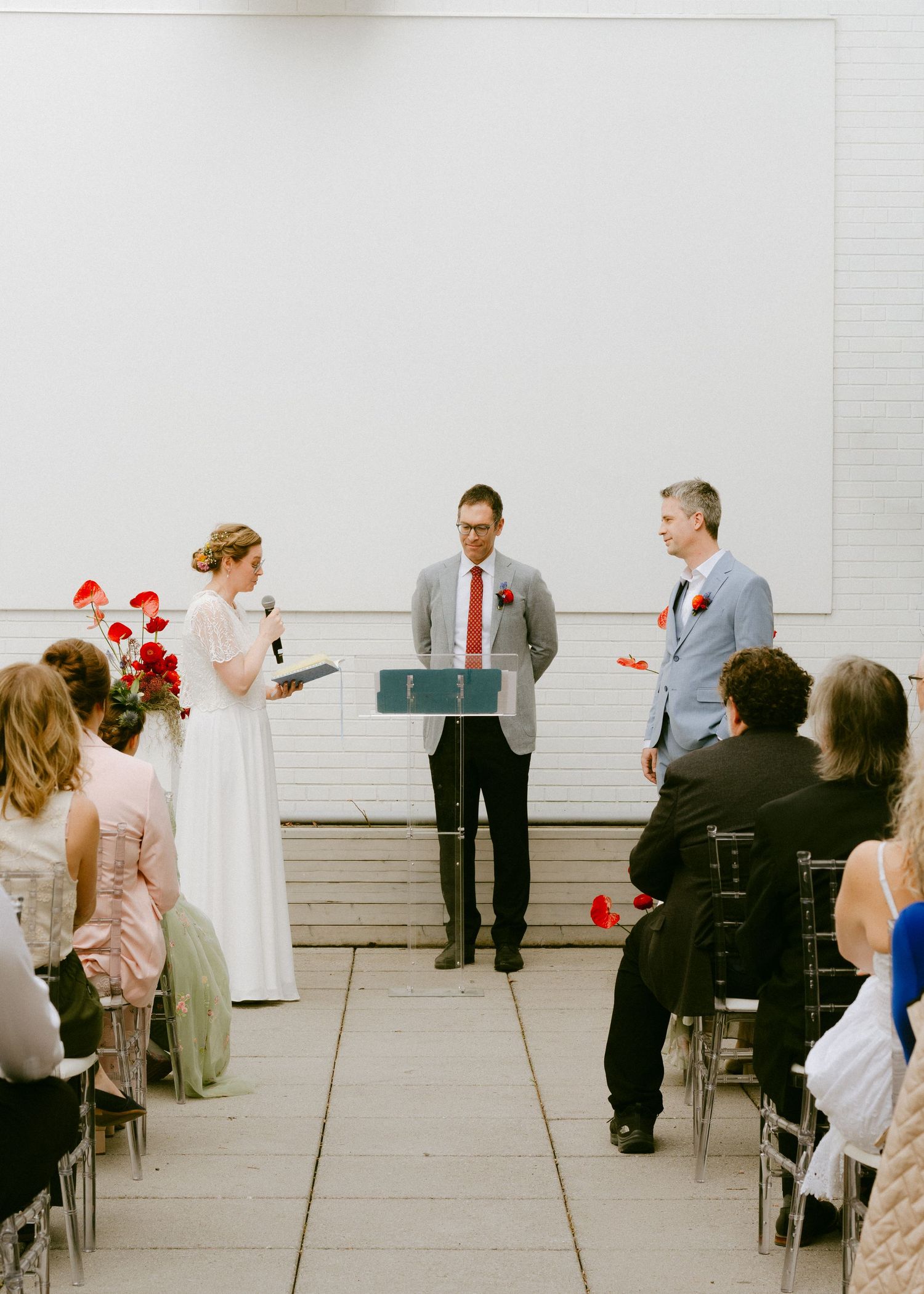 Wedding ceremony on rooftop terrace with bride, groom, and officiant at podium, guests seated in chiavari chairs with red poppy decor.