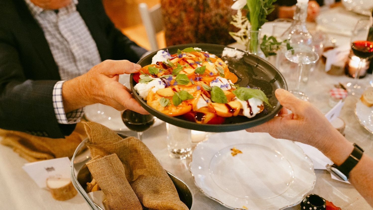 Hands passing a colorful salad dish across a elegantly set wedding reception dinner table.