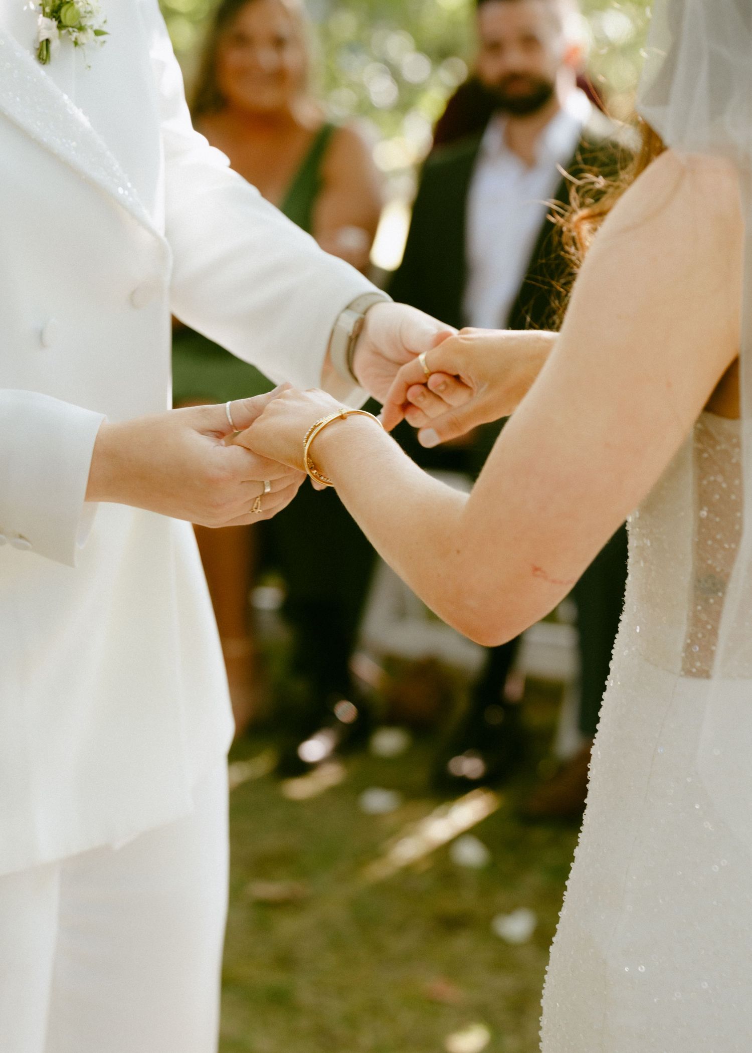 Close-up of two brides holding hands during their outdoor wedding ceremony exchange.