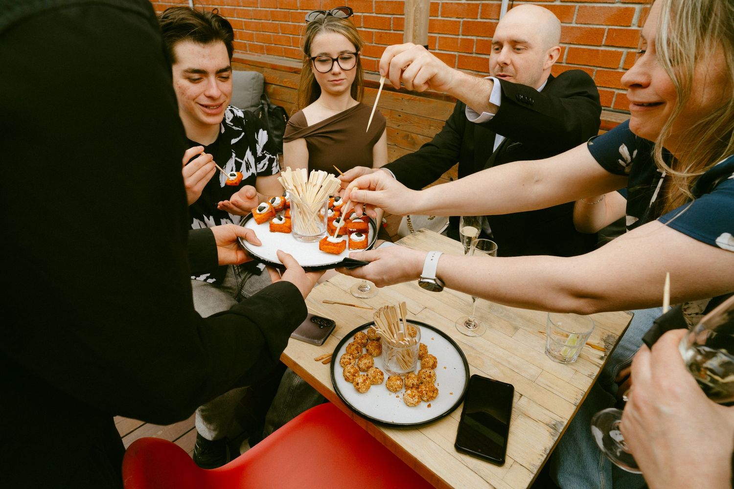 Group of young wedding guests sharing appetizers and finger foods at casual reception table.