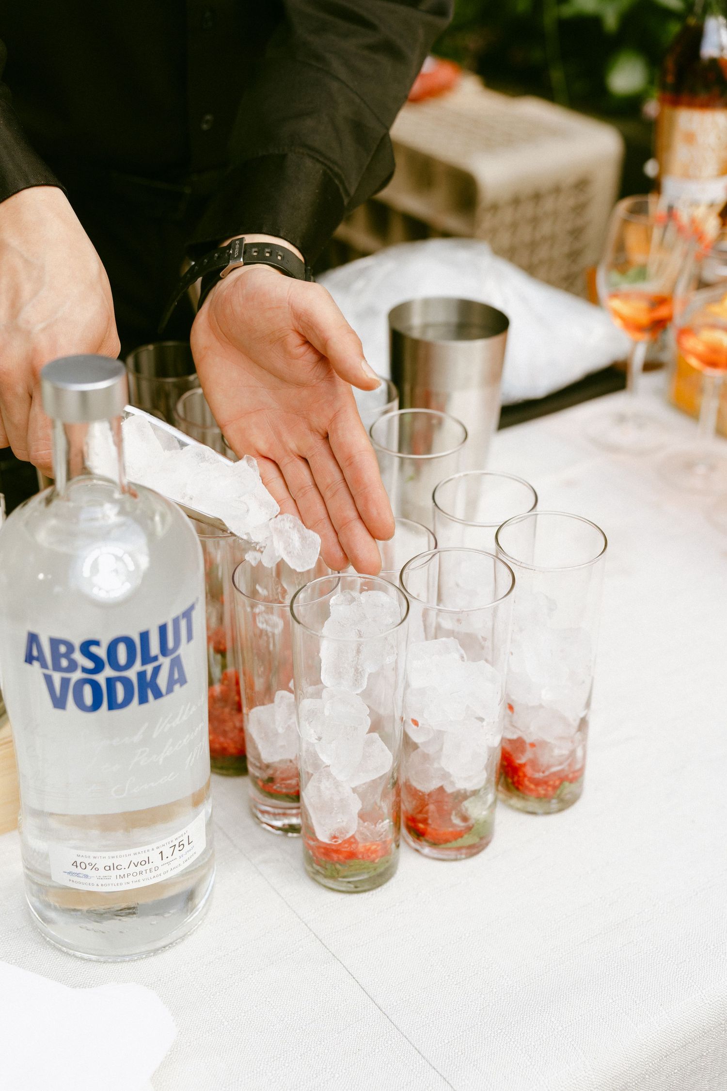 Bartender pouring ice into glasses with strawberries beside a bottle of Absolut Vodka at a wedding bar.