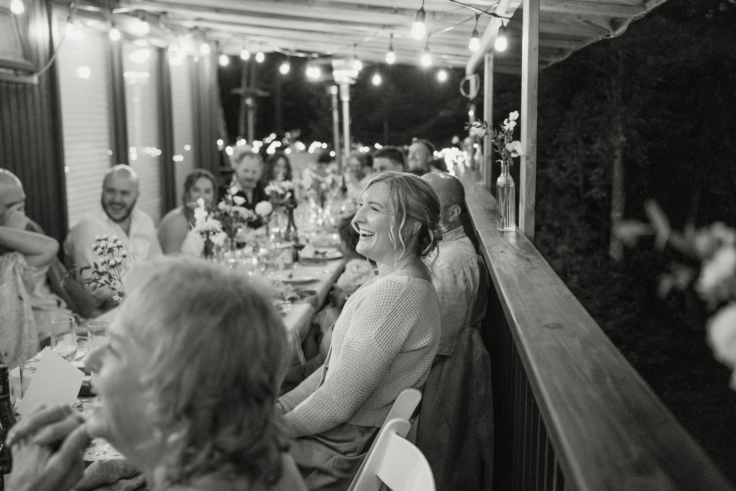 Black and white photo of wedding guests laughing and celebrating at outdoor reception.