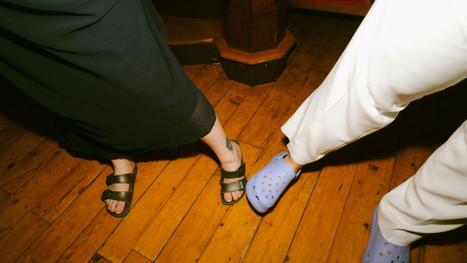 Close-up of wedding guests feet showing contrasting footwear, sandals and blue Crocs on hardwood floor.