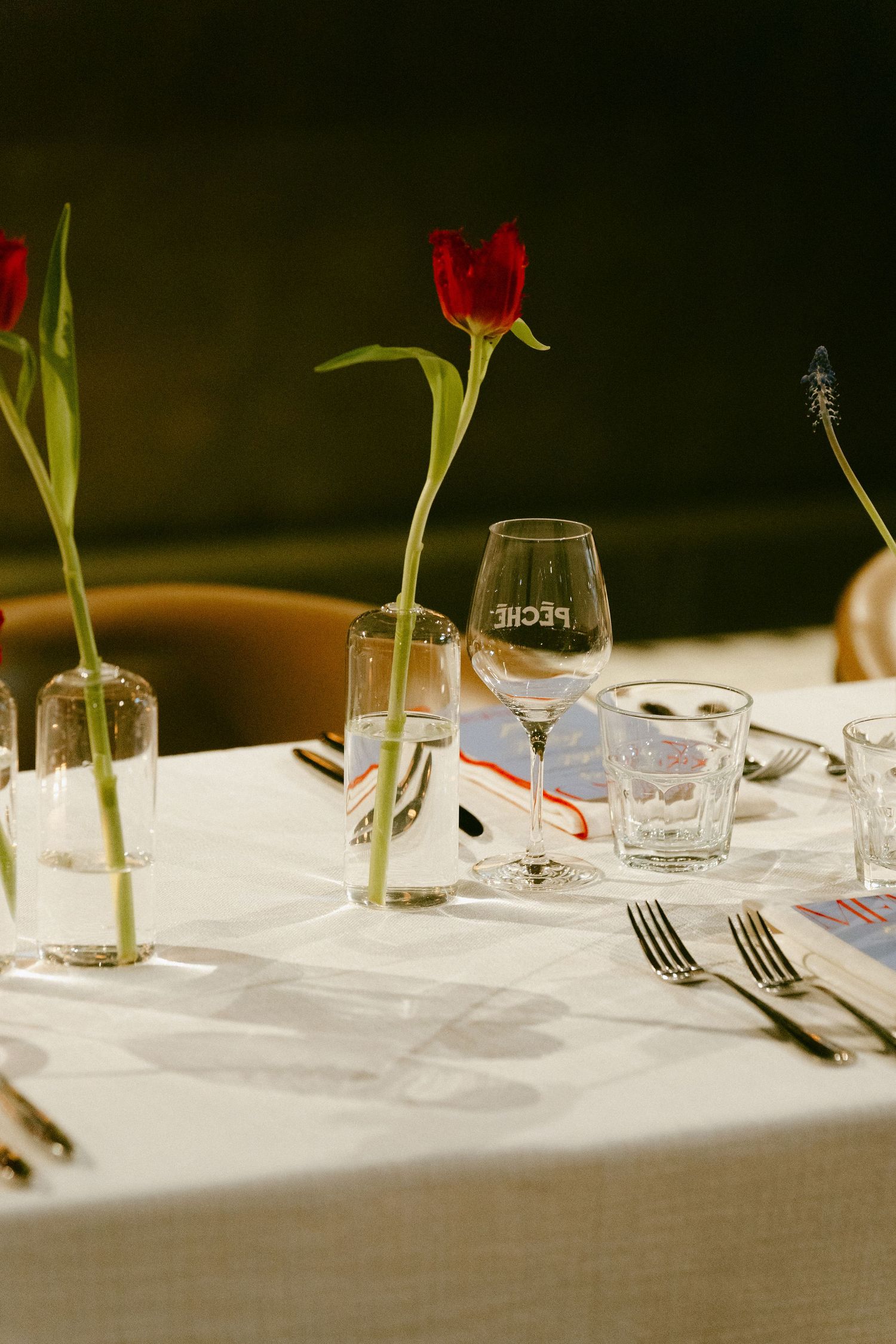 Close-up of wedding reception table with red tulip bud vase and wine glasses.